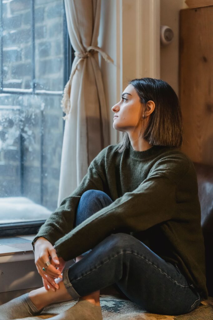 Thoughtful woman standing by a window, reflecting on her own choices and sense of self-worth.